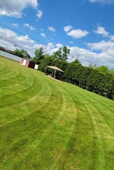 Mowing stripes cut across a large open lawn under a blue sky.